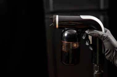 Bir ustanın ellerinde hazır bronzlaşma ekipmanlarının yakın çekimi. Siyah arka plana karşı deri boya sıkmak..