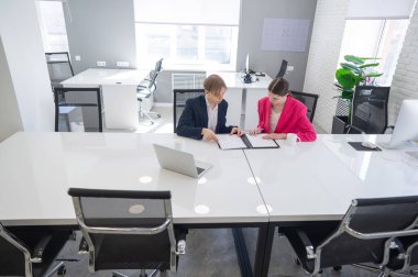 Kadın ve erkek ofiste otururken konuşuyorlar.