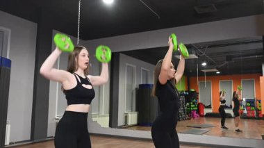 Ağırlık plakalarıyla egzersiz yapan iki beyaz kadın.