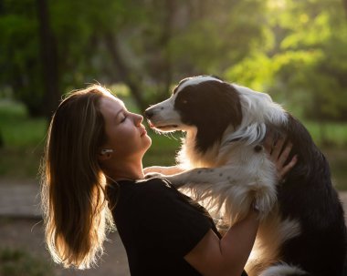 Beyaz bir kadın parkta yürürken köpeğine sarılıyor.