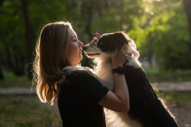 Beyaz bir kadın parkta yürürken köpeğine sarılıyor.