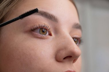 Genç bir kadının dikkatlice maskarasını kirpiklerine sürerken.