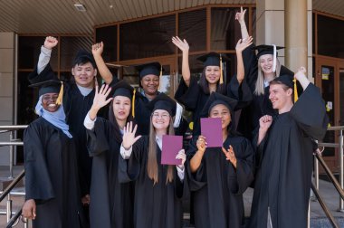 Farklı uluslardan mutlu öğrenciler mezuniyet elbiseleriyle diplomalarını tutuyorlar.