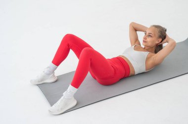 Beyaz arka plan üzerinde karın egzersizi yapan genç bir kadın.