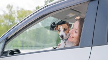 Beyaz kadın köpekle birlikte arabanın camından dışarı bakıyor.