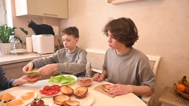 Orta yaşlı beyaz kadın iki oğluyla hamburger pişiriyor.