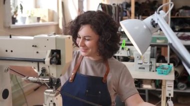 Bir kadın tabakçı dikiş makinesine deri kemer dikiyor.