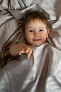 Beyaz tenli şirin bir çocuğun yatakta yatışının üst görüntüsü.