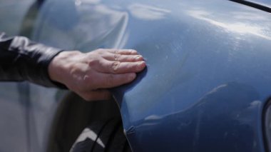 Beyaz adam inceler ve arabasındaki deformasyonu düzeltmeye çalışır.