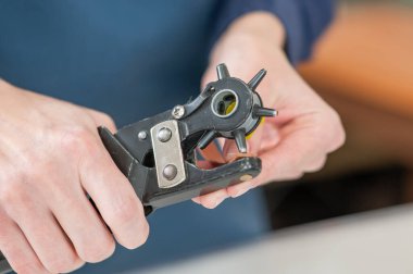 Bir kadın deri kemerde delikler açar. Deri işçileri atölyesi