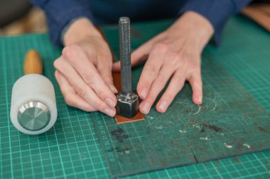 Kadın bronzlaştırıcı bir atölyede deri kemerin kenarlarını inceliyor.