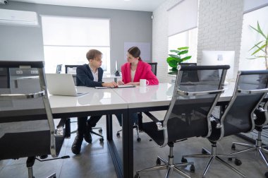 Kadın ve erkek ofiste otururken konuşuyorlar.