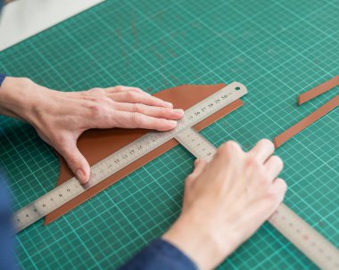 Deri işçisi atölyede deri kesip ölçüyor.