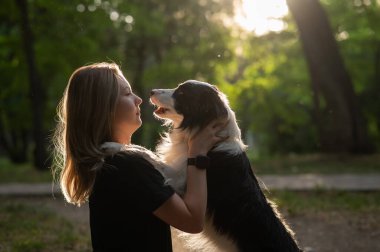 Beyaz bir kadın parkta yürürken köpeğine sarılıyor.