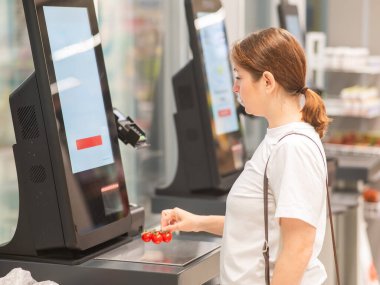 Bir kadın self-servis kasasında vişneli domates tartıyor.