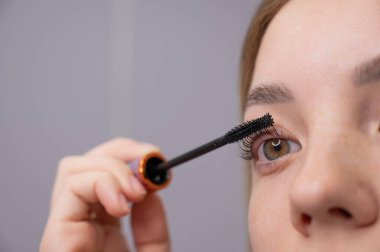 Genç bir kadının dikkatlice maskarasını kirpiklerine sürerken.