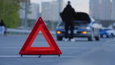 Uyarı üçgeni. Adam çıldırıyor ve arabanın kaputunun altından kablolar koparıyor.