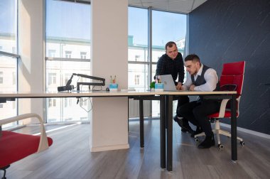 Beyaz adam çalışma masasında durmuş iş hakkında konuşuyor.