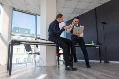 Ofiste iş tartışan iki beyaz adam. İşitme cihazı olan bir iş adamı.