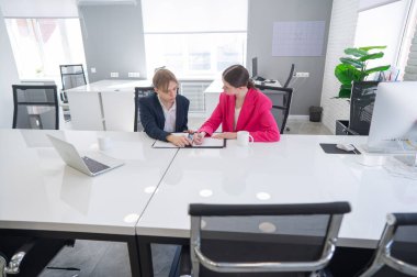 Kadın ve erkek ofiste otururken konuşuyorlar.