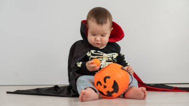 Beyaz arka planda şeker sepeti tutan Dracula Cadılar Bayramı kostümlü beyaz tatlı çocuk.