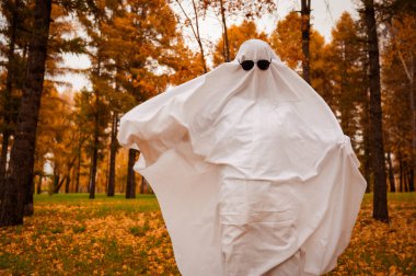 Bir sonbahar ormanının arka planında hayalet kostümlü bir kadın. Cadılar Bayramı kostümü