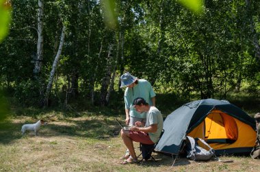 Kamp yaparken dizüstü bilgisayarda çalışan beyaz bir adam. Çift doğada dinleniyor.