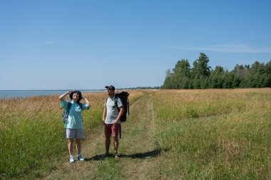 Kafkasyalı çift deniz kıyısında sırt çantalarıyla yürüyüş yapıyor.
