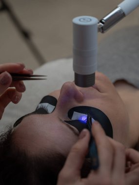 Kirpik uzatma prosedüründen geçen bir kadın ultraviyole lamba kullanıyor.