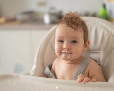 Ekşi kremaya bulanmış sevimli erkek bebek yüksek bir sandalyede oturuyor.