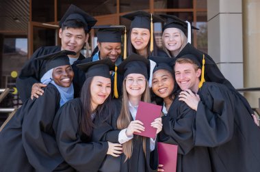Farklı uluslardan mutlu öğrenciler mezuniyet elbiseleriyle diplomalarını tutuyorlar.