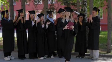 Sınıf arkadaşları onu alkışlarken, elinde diploma tutan beyaz bir kadın.