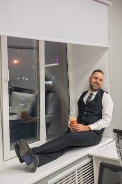 Ofisteki pencere eşiğinde oturan düşünceli beyaz adam.