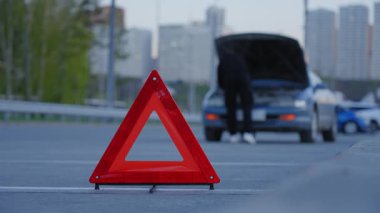 Uyarı üçgeni. Adam çıldırıyor ve arabanın kaputunun altından kablolar koparıyor.