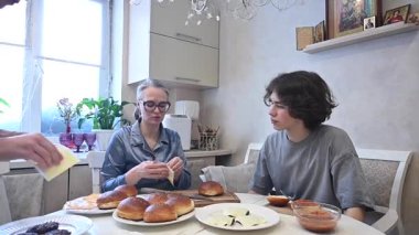 Orta yaşlı beyaz kadın iki oğluyla hamburger pişiriyor.