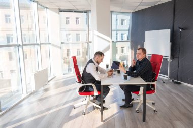 Masada otururken akıllı telefon kullanan iki beyaz adam.