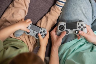 Beyaz kadın küçük oğluna konsol oynamayı öğretiyor. Oyun kolu ellerinde.