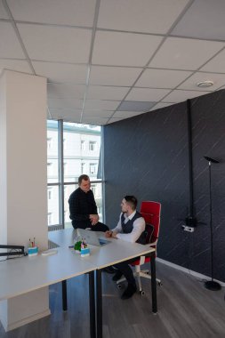 Beyaz adam çalışma masasında durmuş iş hakkında konuşuyor.