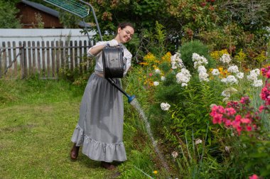 Bahçede çiçekleri sulayan beyaz bir kadın.