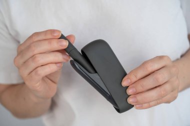 Bir kadın, tütün ısıtma sistemini şarj aletinden çıkarır. Elektronik sigara.