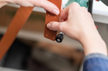 Deri işçisi atölyede kemer için deri şeritlerini öğütüyor.