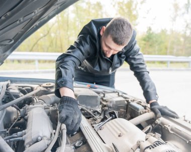 Bir adam arabasındaki bujileri değiştirir.