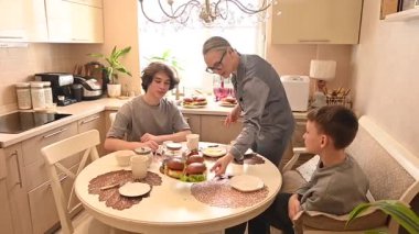 Orta yaşlı beyaz bir kadın iki oğluyla yemek yiyor. Aile çay partisi.