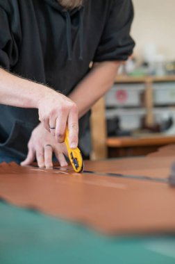 Deri işçisi atölyede deri kesip ölçüyor.