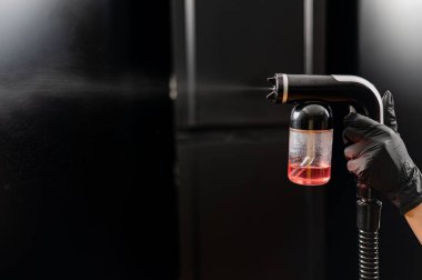 Bir ustanın ellerinde hazır bronzlaşma ekipmanlarının yakın çekimi. Siyah arka plana karşı deri boya sıkmak..