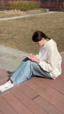 Açık havada kalemle çizim yapan beyaz bir kadın.