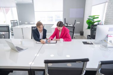 Kadın ve erkek ofiste otururken konuşuyorlar.