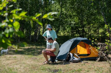 Kamp yaparken dizüstü bilgisayarda çalışan beyaz bir adam. Çift doğada dinleniyor.