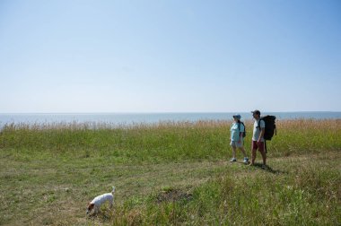 Kafkasyalı çift deniz kıyısında sırt çantalarıyla yürüyüş yapıyor.