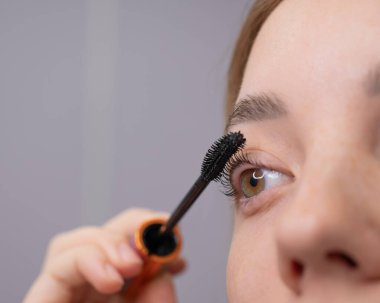Genç bir kadının dikkatlice maskarasını kirpiklerine sürerken.